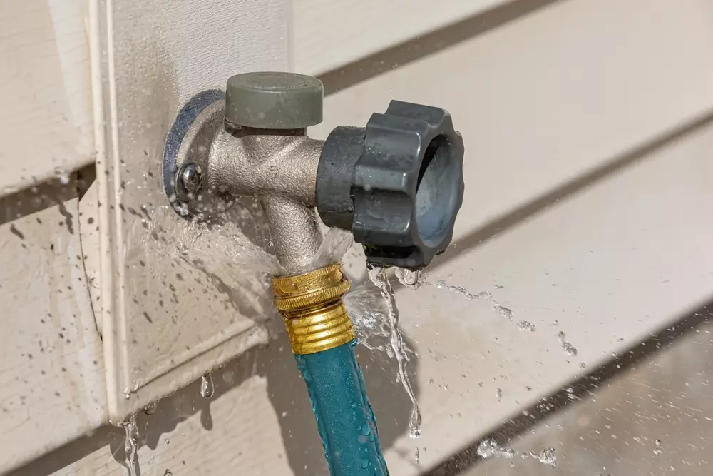 Leaky outdoor water spigot spraying water around a connected garden hose, signaling the need for repair or maintenance.